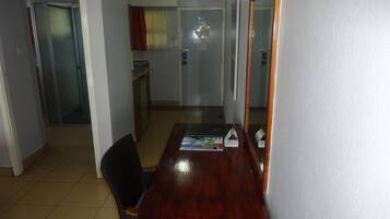 A room with a wooden dining table, two chairs, a small kitchen area, and a door leading to another room.