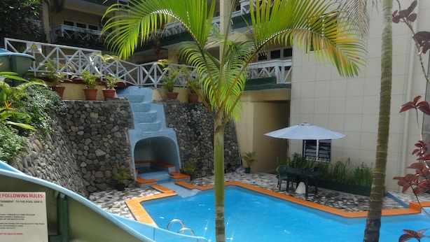 A swimming pool with a water slide, surrounded by potted plants and a stone wall. - Suva Motor Inn (Suva)