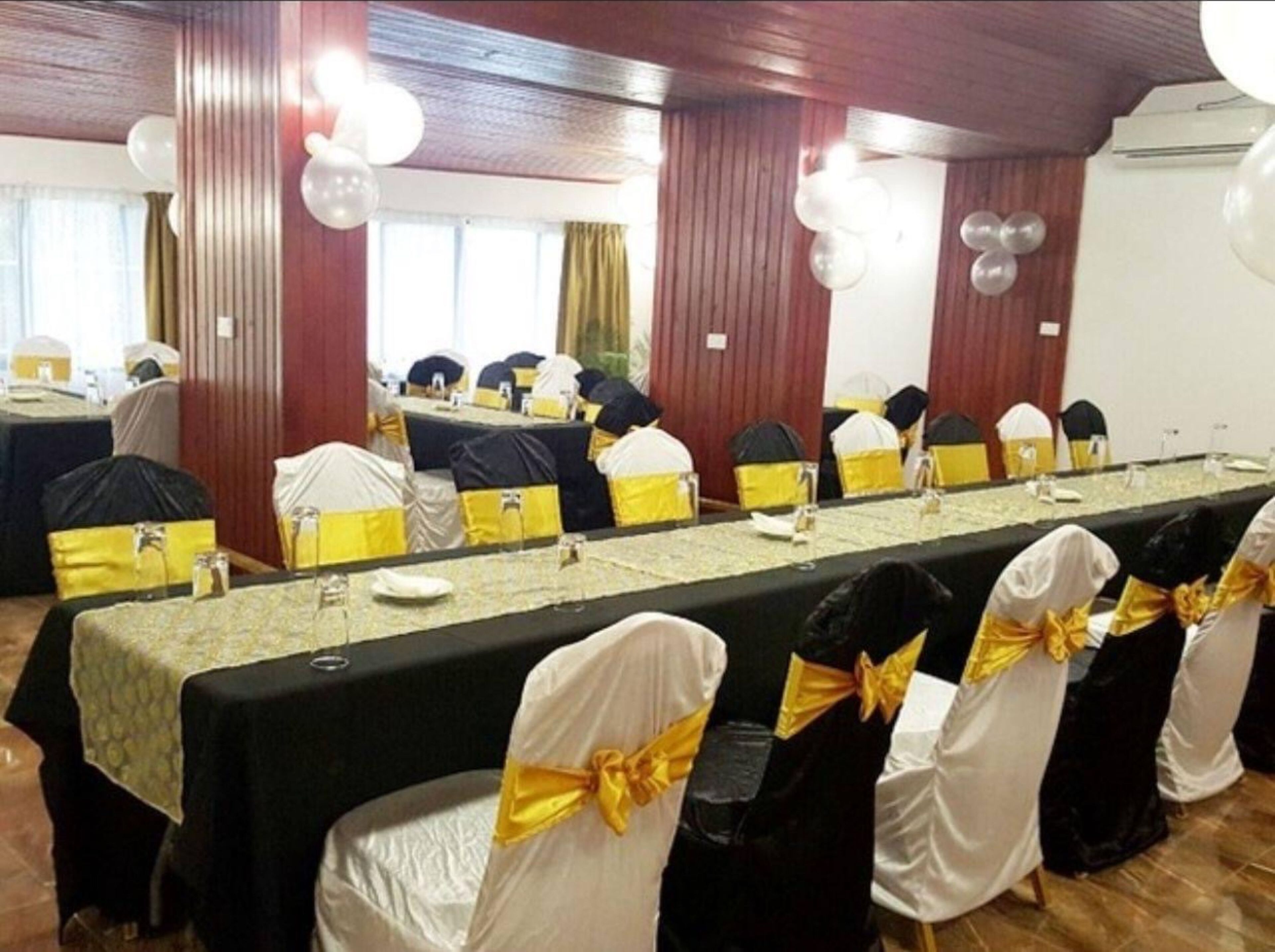 Un salón de conferencias con una larga mesa, sillas adornadas con cintas amarillas y globos.