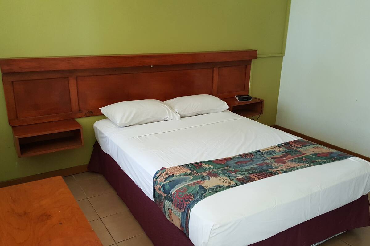A single bed with a wooden headboard, white bedding, and a colorful throw blanket.