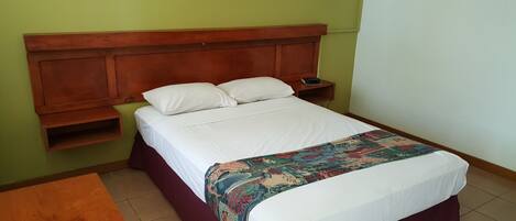 A single bed with a wooden headboard, white bedding, and a colorful throw blanket.