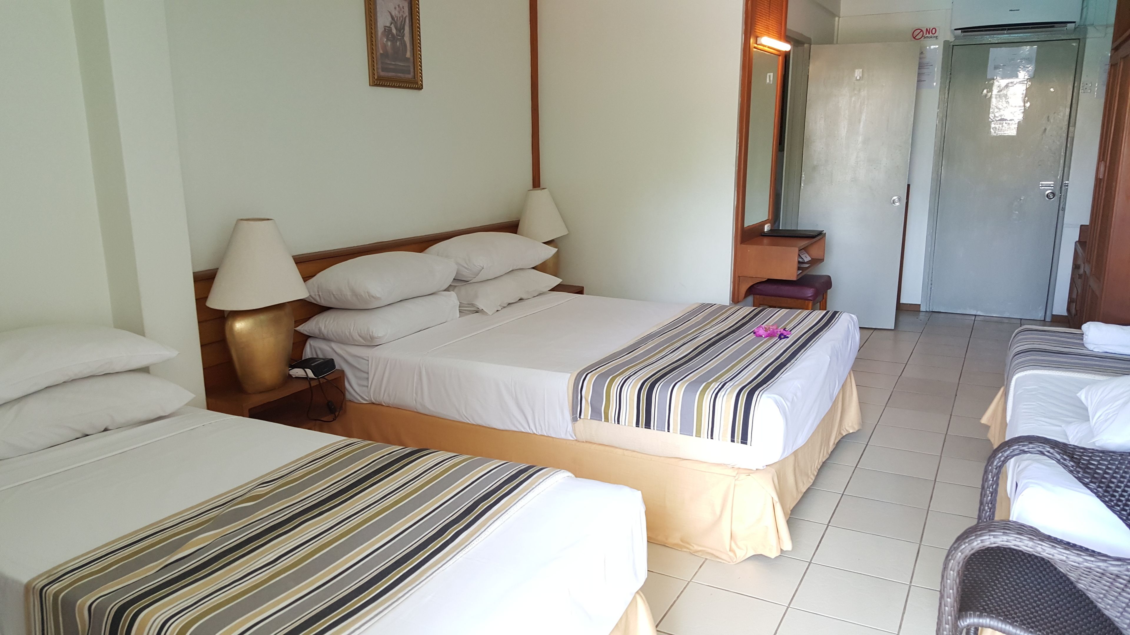 Habitación de hotel con dos camas, una mesita de noche con lámpara, cabecero de madera, espejo y una puerta.