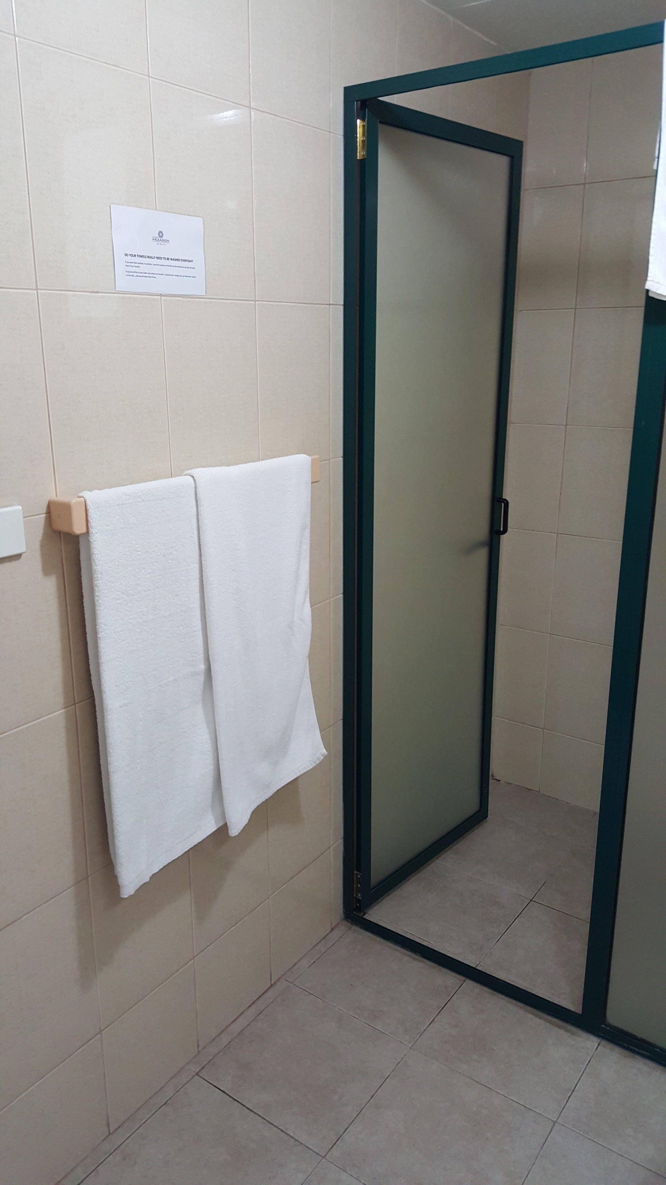 Un baño con mampara de ducha, dos toallas colgadas en un perchero y un cartel en la pared.