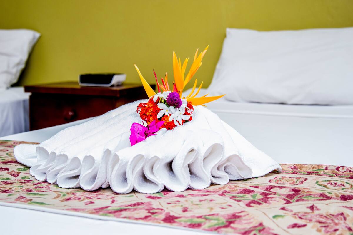 A neatly folded white towel with a floral arrangement on a bed with a floral-patterned bedspread.