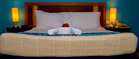 A hotel room with a large bed, two bedside lamps, a telephone, and a decorative rose on the pillow.