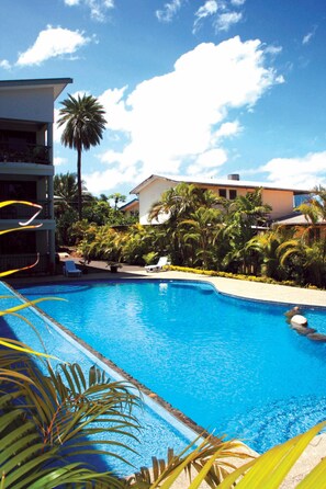 A swimming pool surrounded by palm trees and a building with a balcony. - Hexagon International Hotel (Nadi)