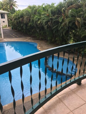 A swimming pool with a metal railing, surrounded by lush greenery and a building in the background. - Hexagon International Hotel (Nadi)