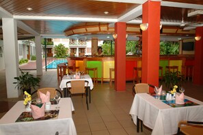 A restaurant with tables set for dining, a bar area, and a pool visible in the background. - Hexagon International Hotel (Nadi)