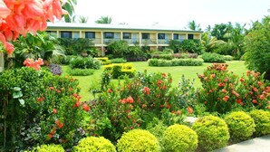 A hotel with a green lawn, red flowers, and various shrubs. - Grand West's Villas (Nadi)