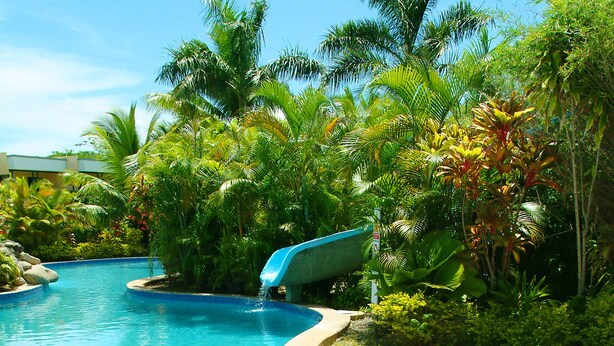 A swimming pool with clear blue water, surrounded by tropical vegetation and rocks. - Grand West's Villas (Nadi)