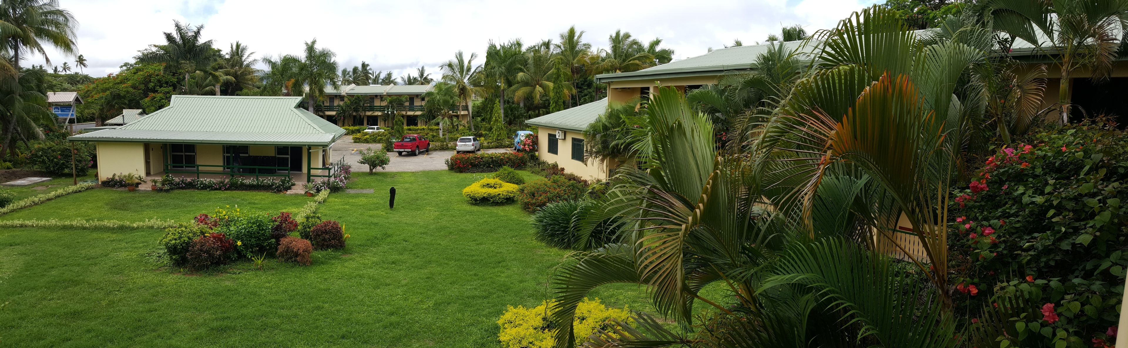 A hotel with a green roof, surrounded by lush gardens and palm trees.