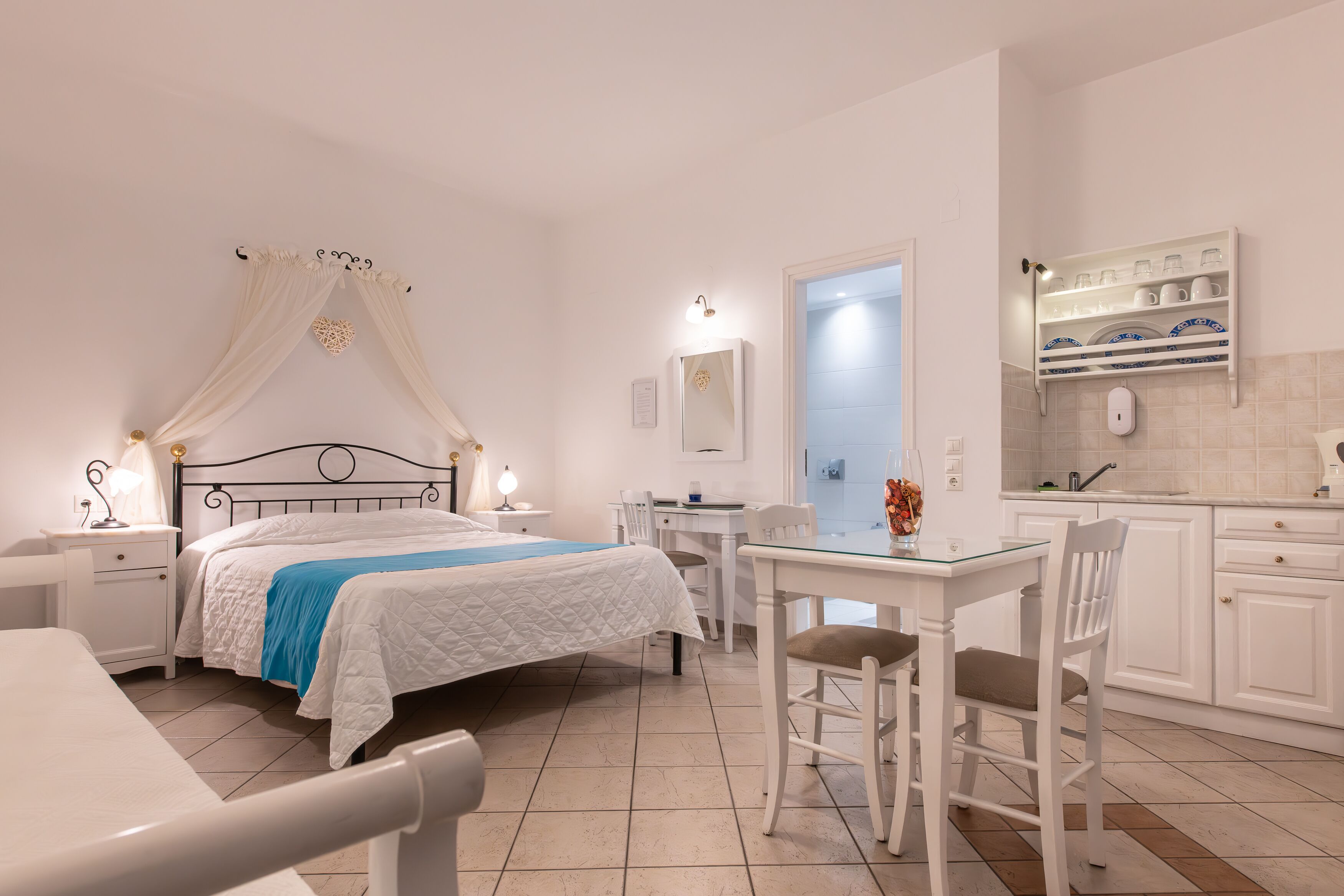 Un dormitorio con cama, mesitas de noche, un escritorio y una silla. Incluye un baño con lavamanos y espejo.