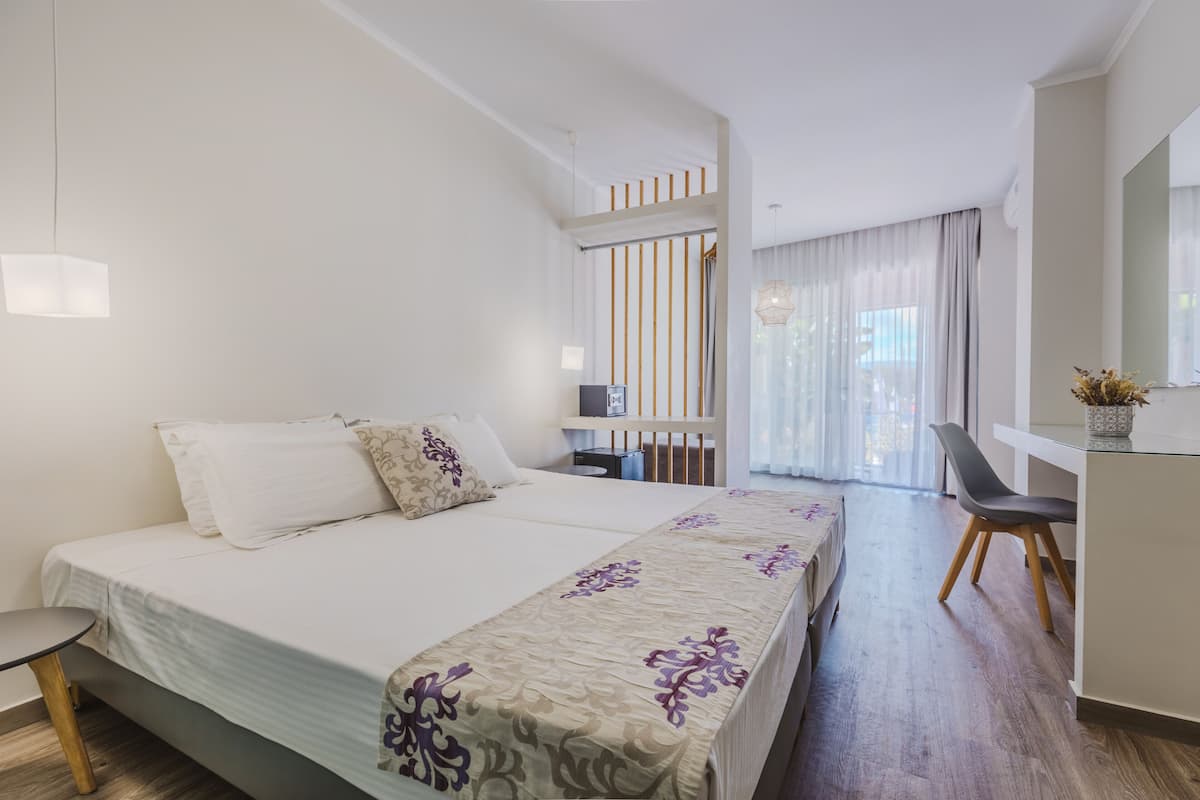 Une chambre d’hôtel moderne avec un grand lit, un bureau et une chaise. Il y a une fenêtre avec des rideaux, une petite table et une plante sur le bureau.