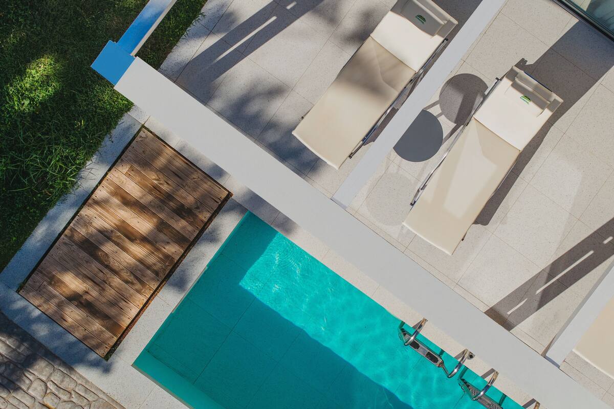 Vue aérienne d’un espace piscine moderne, avec une terrasse en bois, une piscine et des chaises longues.