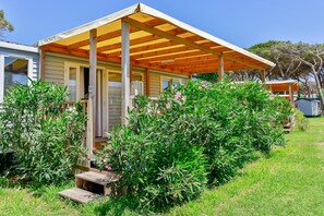A single-story house with a porch, surrounded by greenery and a clear blue sky.