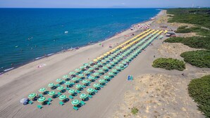 Luchtbeeld van een strand met rijen parasols en ligbedden, een heldere lucht en de oceaan.