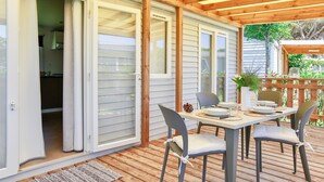 Een overdekt terras met een tafel voor twee personen, schuifdeuren naar een keuken en een houten terras met een leuning.