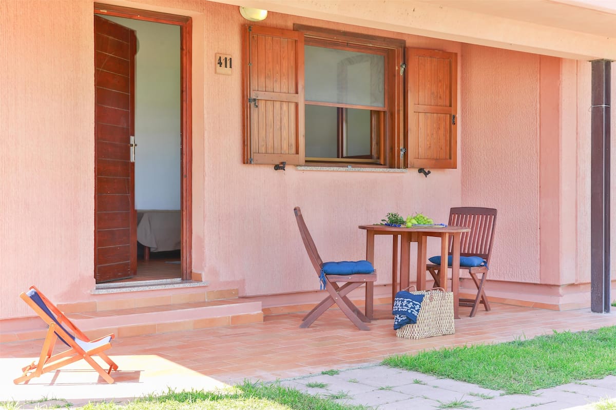 Une pièce avec une porte en bois, une fenêtre avec des volets, une table avec des chaises et une petite table sur laquelle se trouve une plante.