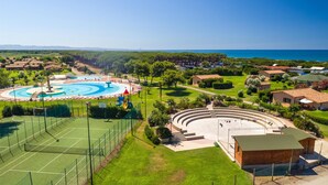Een groot buitenbad met een rond ontwerp, omringd door een tennisbaan en een klein openluchttheater.