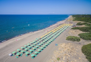 An aerial view of a beach with rows of umbrellas and sun loungers, a clear sky, and the ocean.