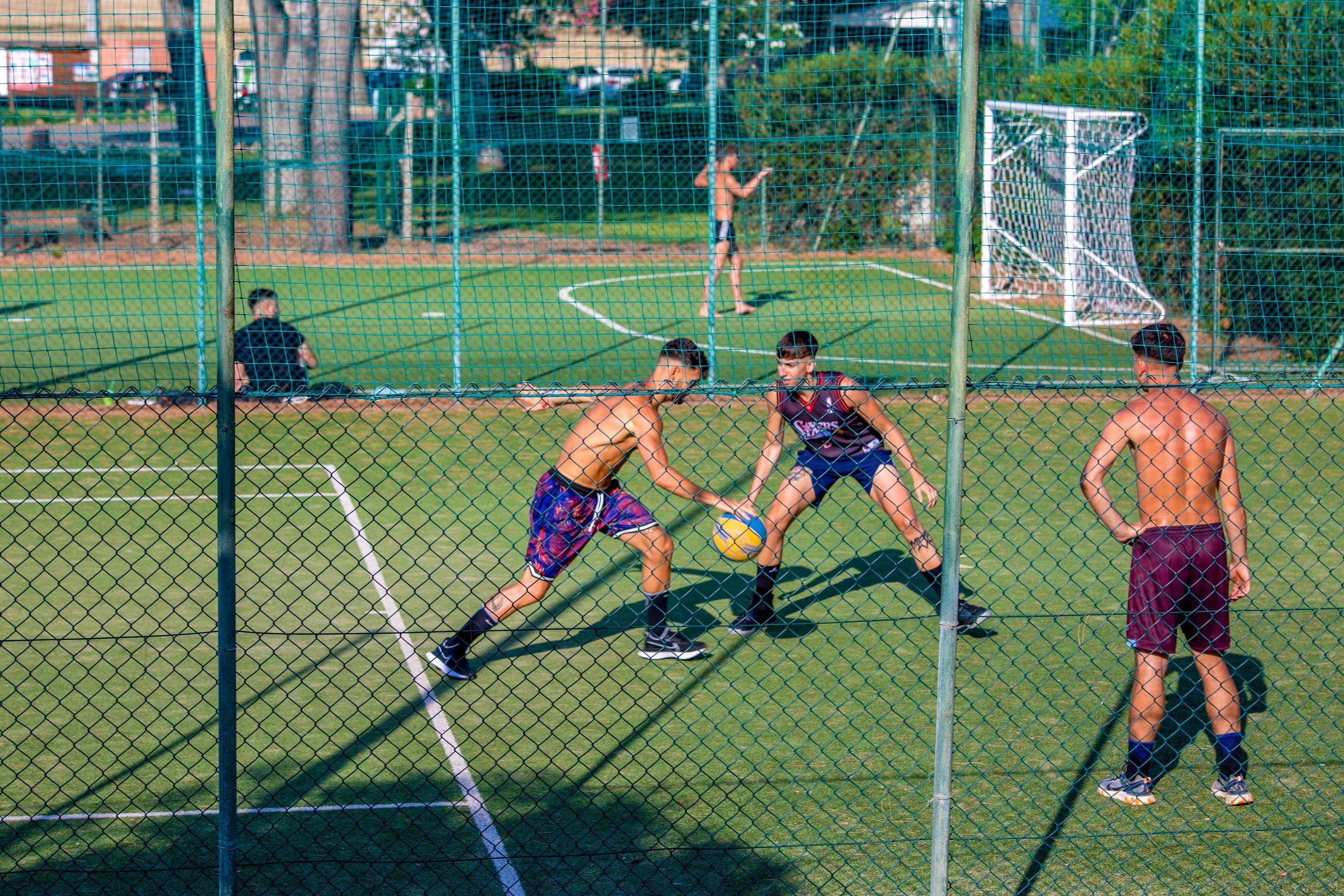 Un terrain de sport entouré d’un filet, avec des poteaux de but et des joueurs.