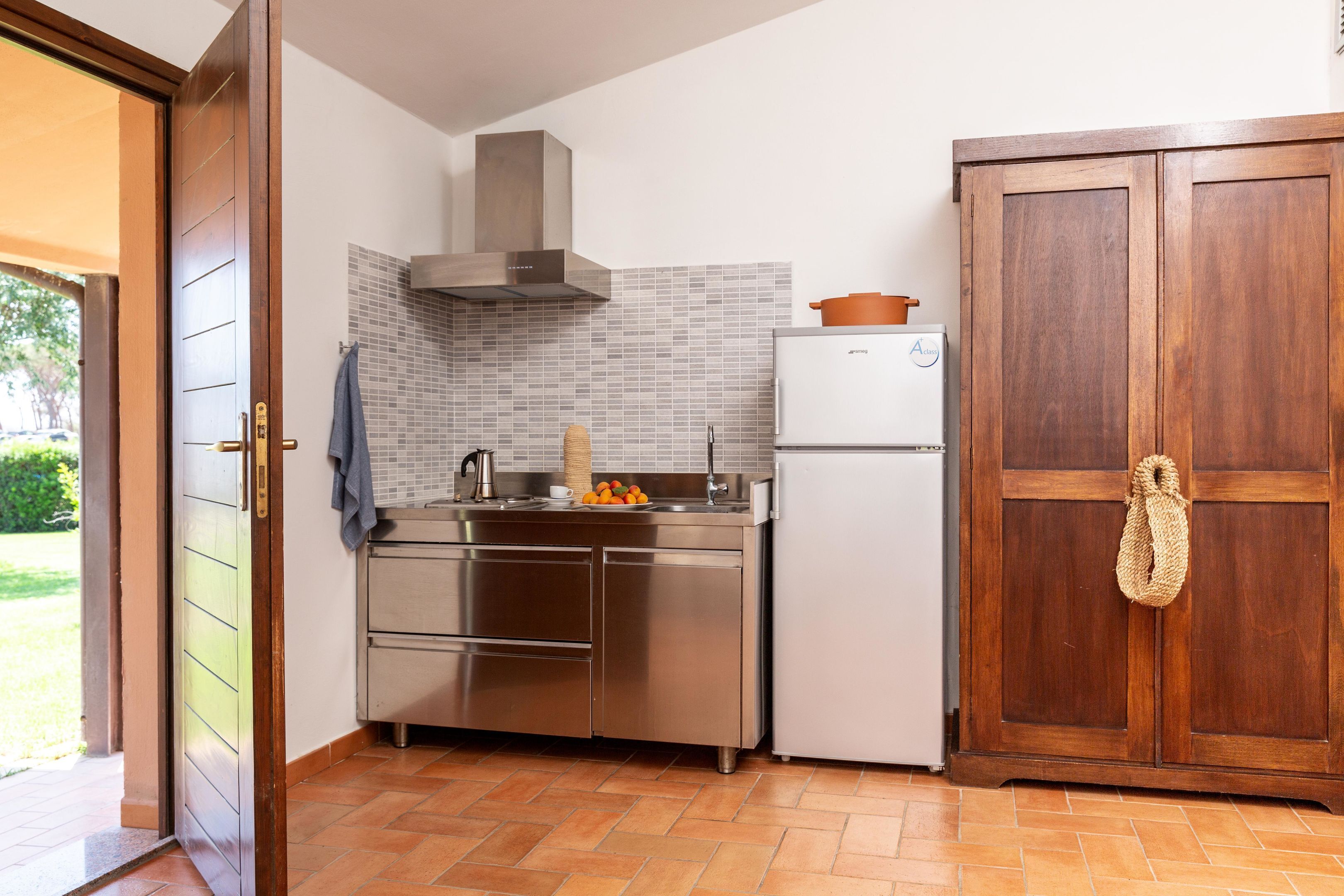 A compact kitchen with a stainless steel refrigerator, a built-in oven, and a wooden cabinet.