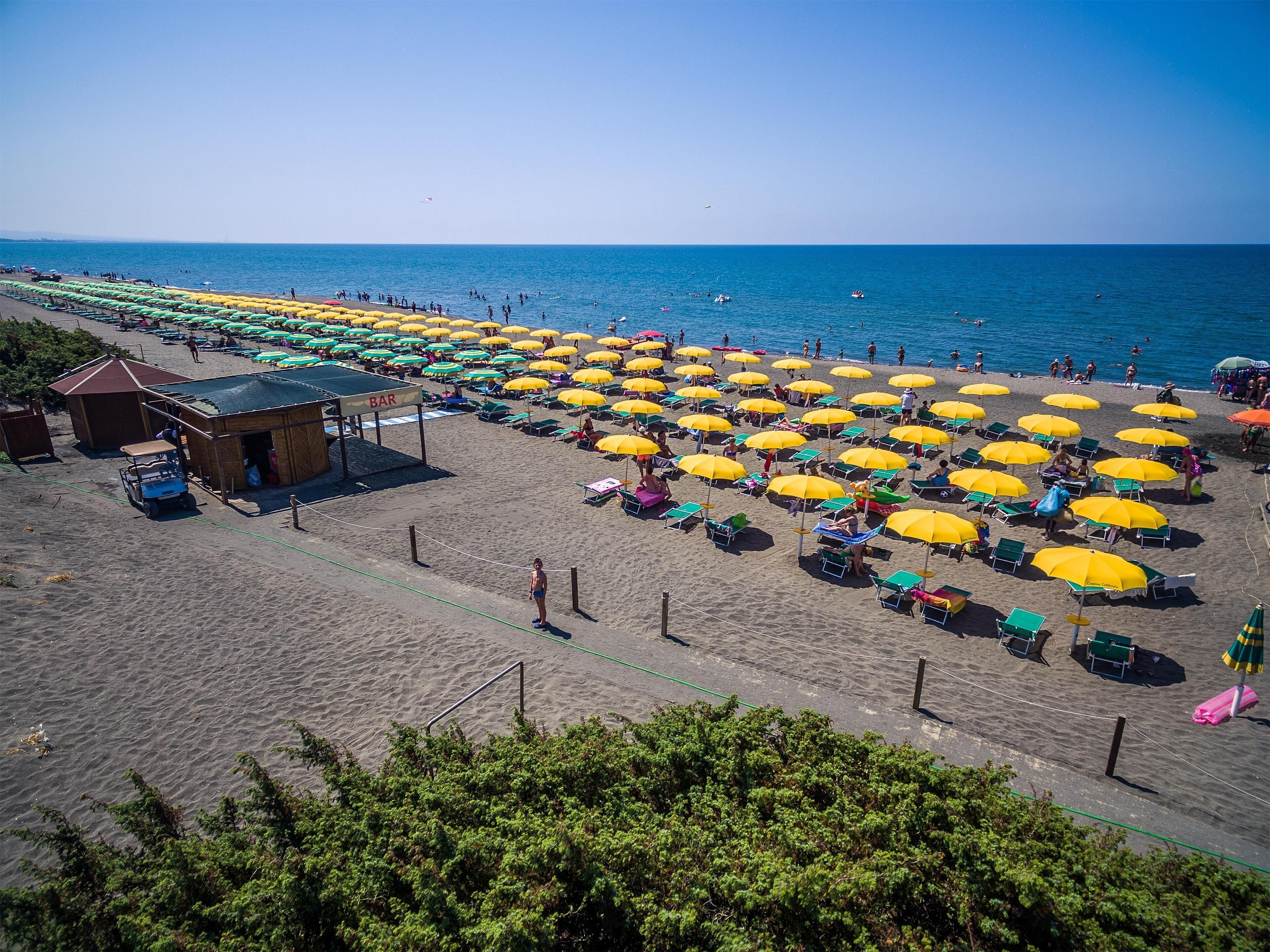 Une vue aérienne d’une plage avec des rangées de parasols et de chaises longues, un bar et un petit bâtiment.