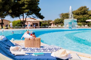 A poolside area with lounge chairs, a wicker basket, a book, and a hat.