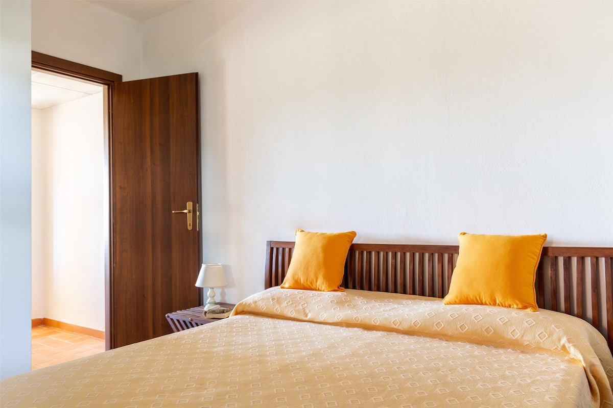 Un lit bien fait, avec une couvre-lit à motifs et deux oreillers, une tête de lit en bois et une table de chevet avec une lampe.