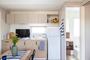A compact kitchen with a stove, sink, and refrigerator, a dining area with a table and chairs, and a small window providing natural light. - Gitavillage California (Montalto di Castro)