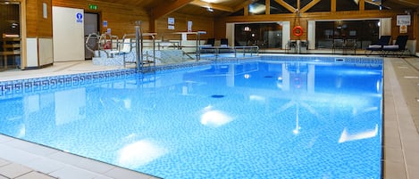 An indoor swimming pool with tiled walls and ceiling, clear signage, and a lifeguard chair.