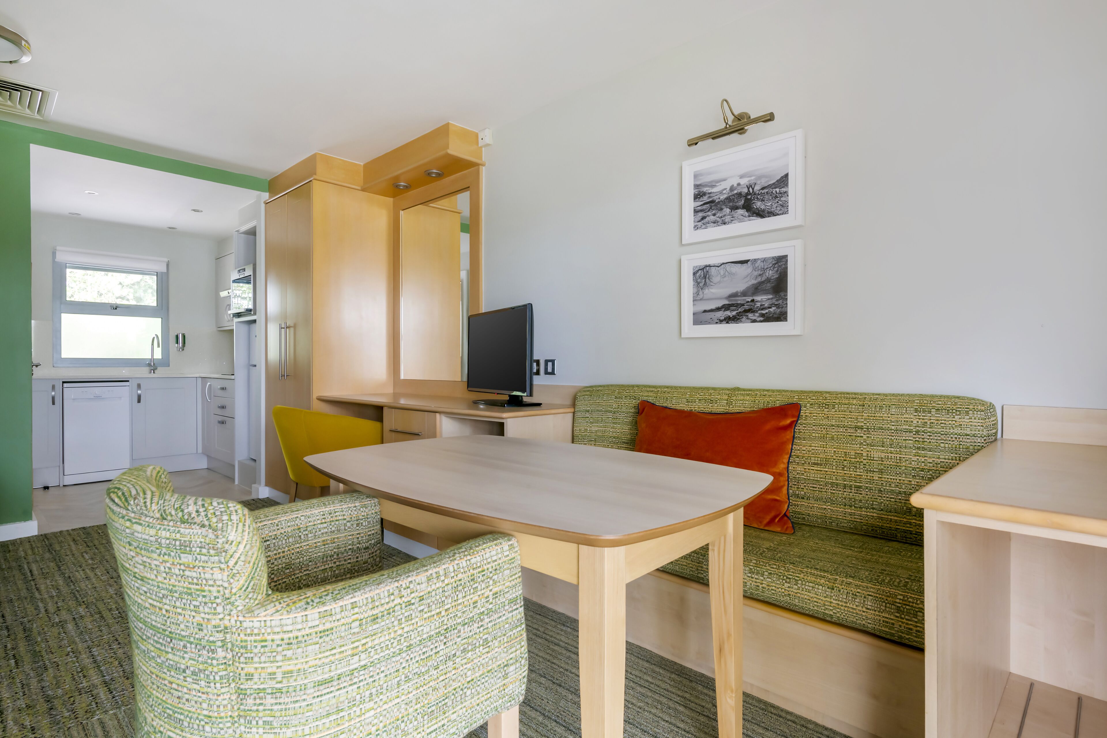 Un espacio habitable compacto con kitchenette, zona de comedor y un sofá con un cojín rojo.