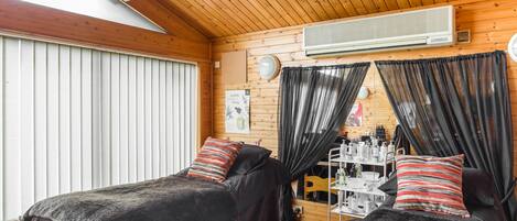 A cozy cabin room with two beds, wooden walls, a ceiling fan, and a window with blinds.