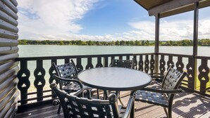 A covered outdoor deck with a table and chairs, overlooking a lake with buildings in the distance. - Pine Lake Resort (Carnforth)