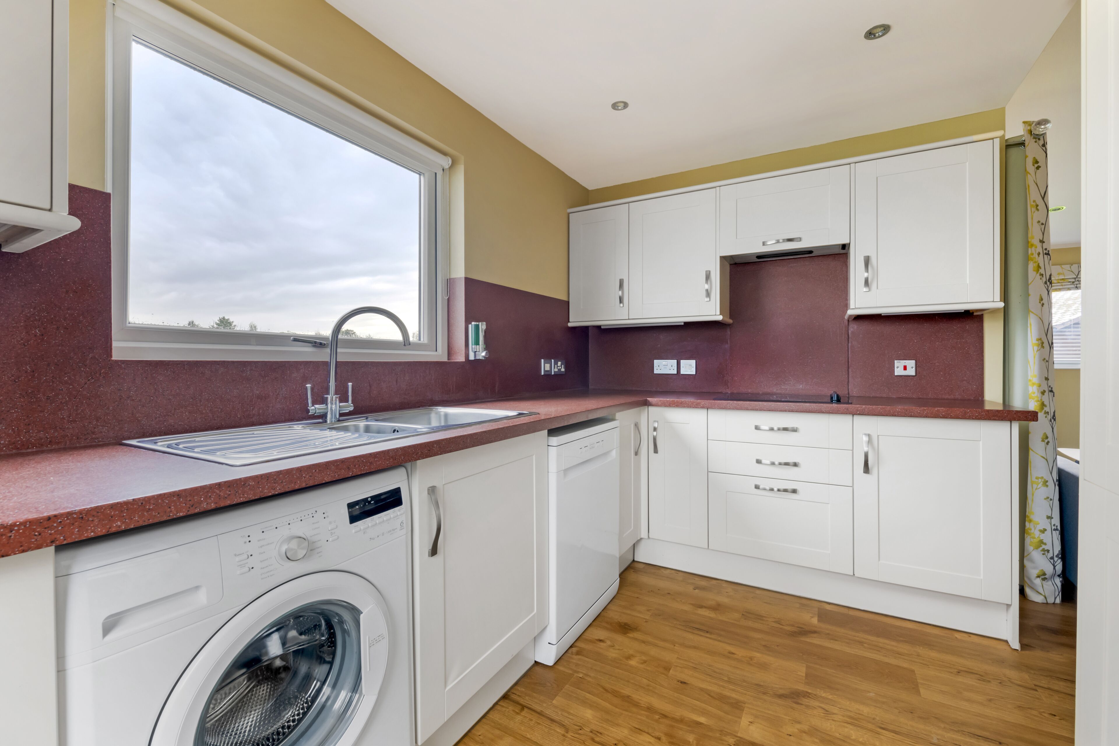 A modern kitchen with a built-in washer, a window, and wooden flooring.