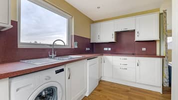 A modern kitchen with a built-in washer, a window, and wooden flooring.