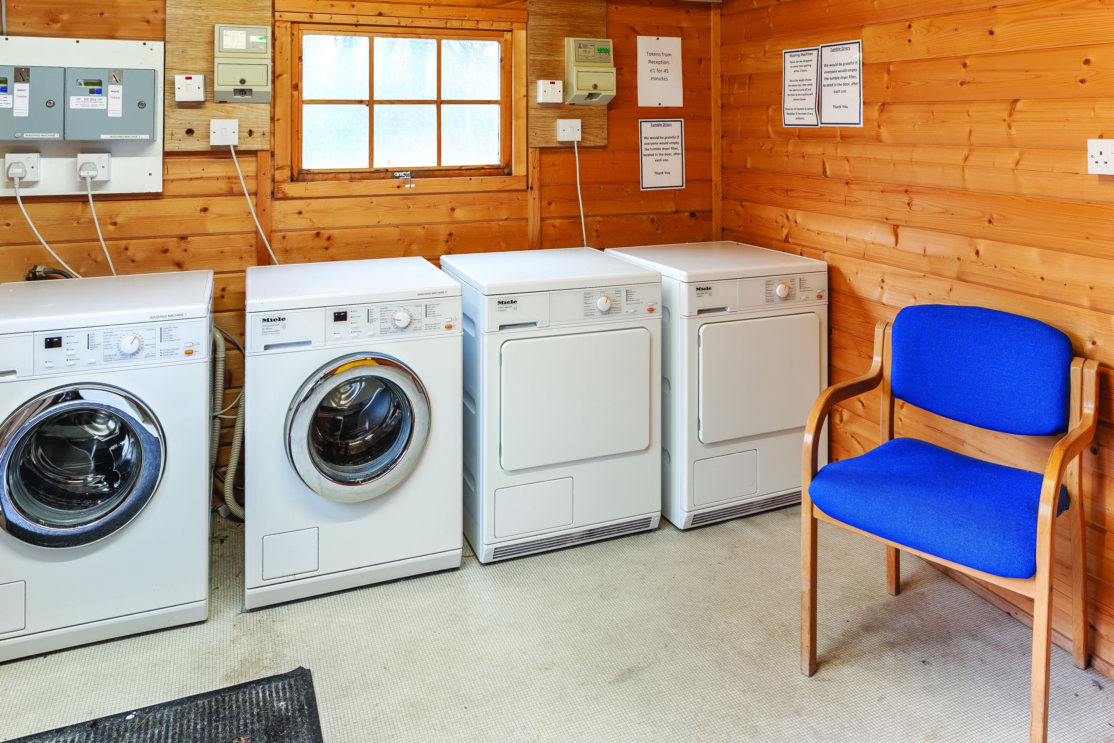 A laundry room with three washing machines and a blue chair.