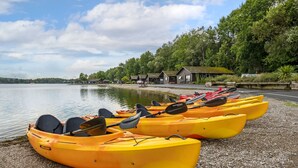 A row of yellow kayaks lined up on a pebbled shore by a calm lake, with a row of cabins in the background. - Pine Lake Resort (Carnforth)