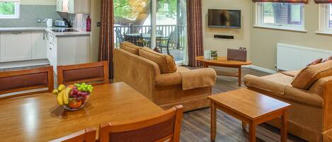 A modern living room with a sofa set, a dining table with fruit, and a kitchen area with cabinets and a TV.