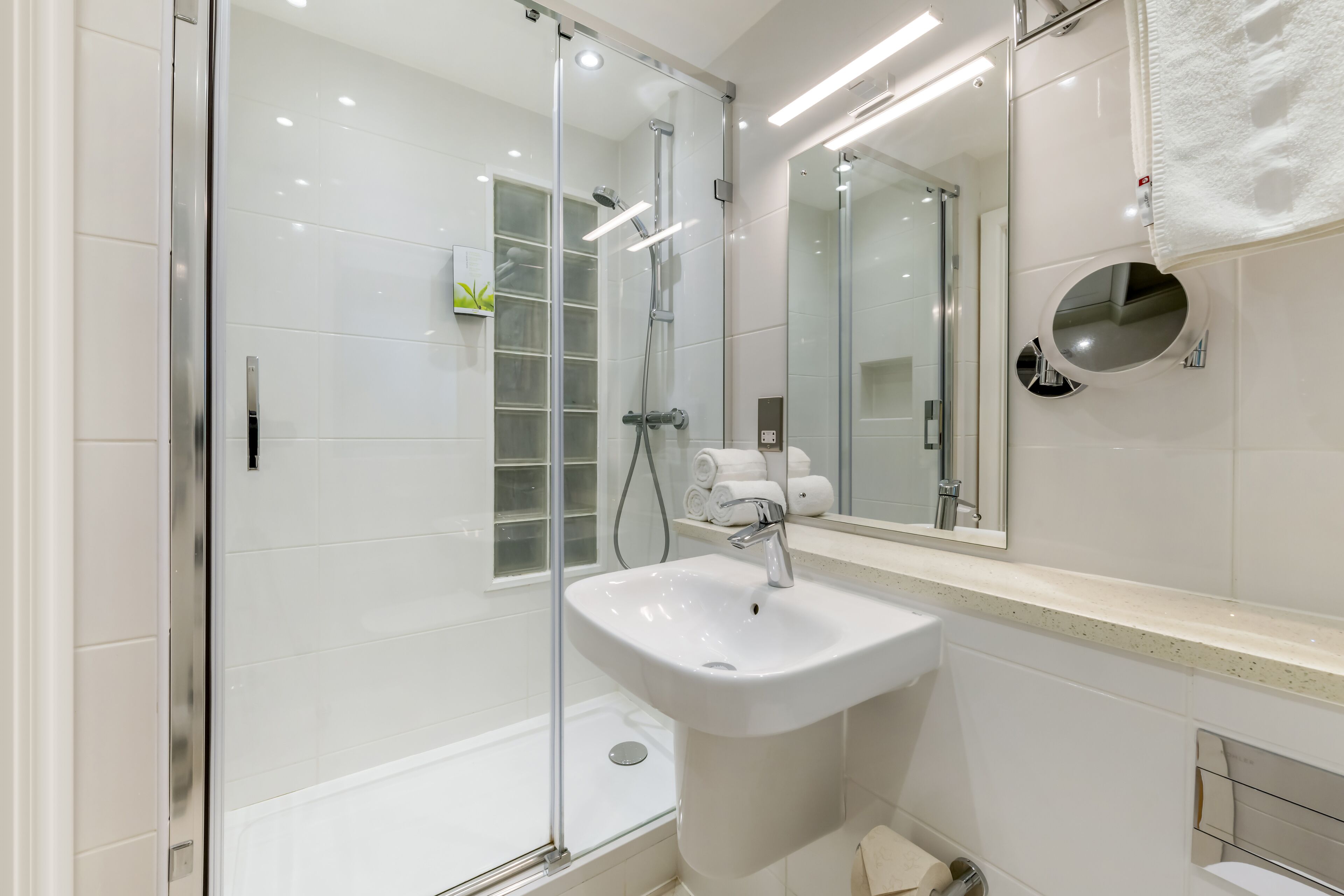 Een moderne badkamer met een douchecabine van glas, een witte wastafel en een grote spiegel.