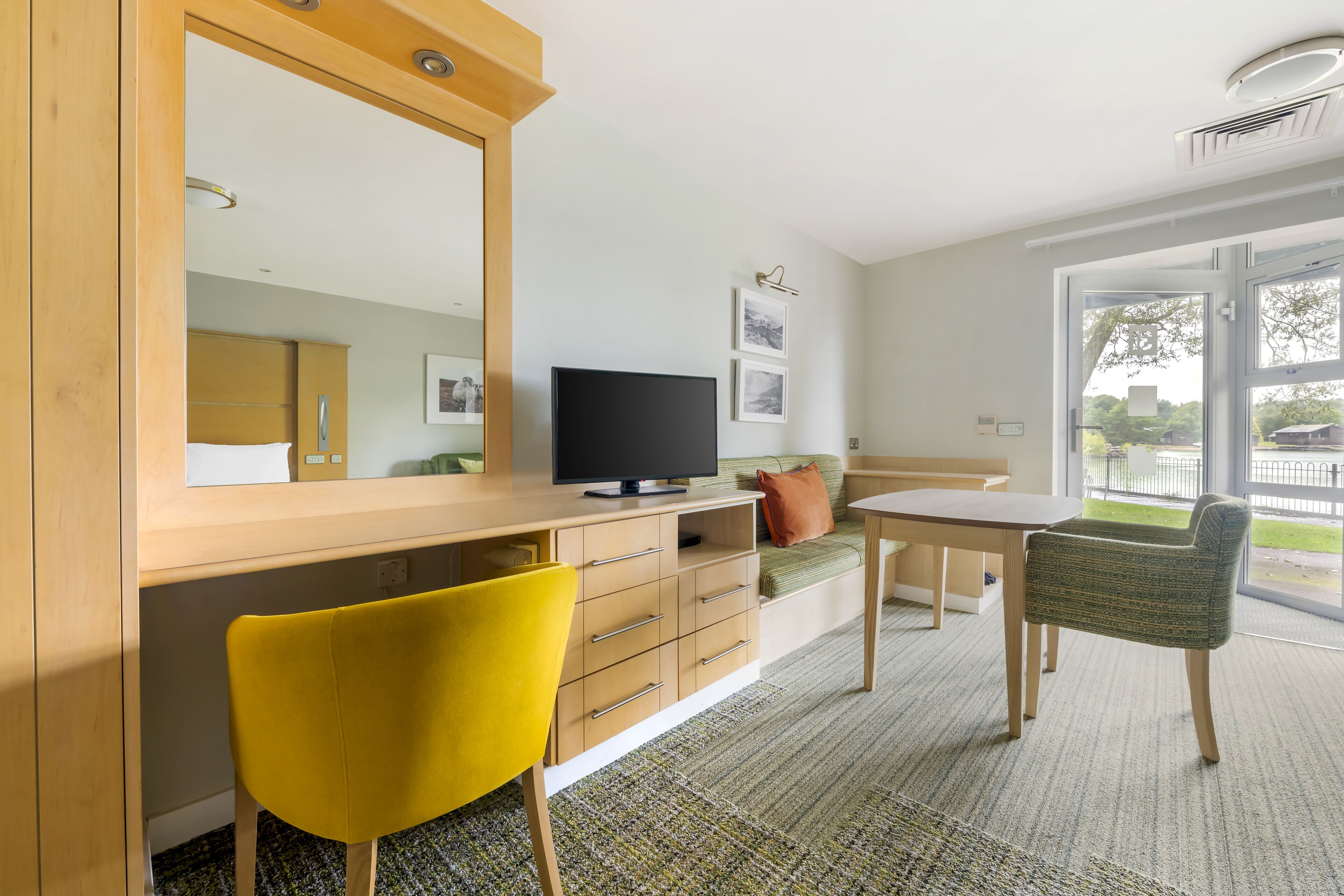 A modern room with a wooden desk, a television, a sofa, and a dining table.