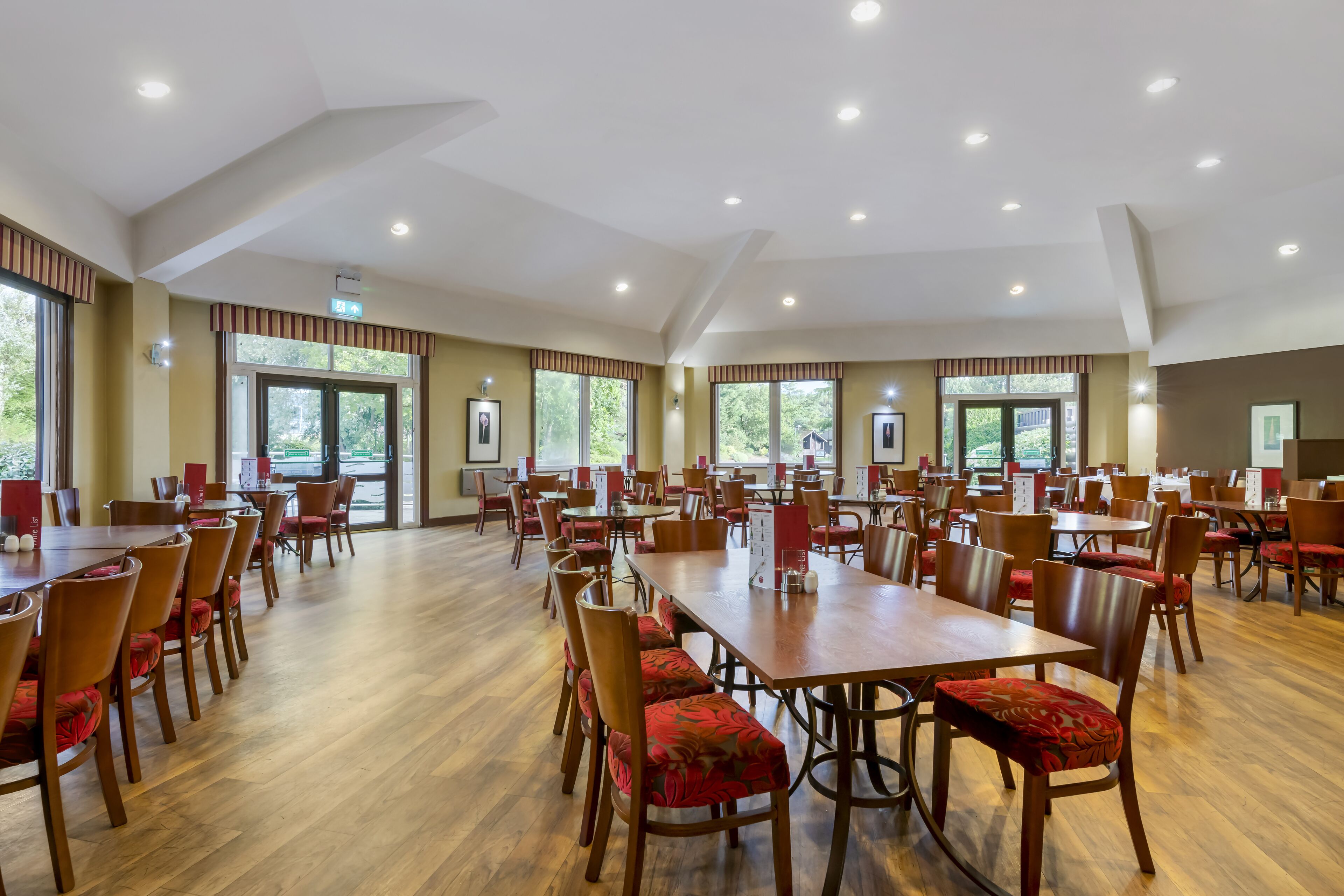 Un vaste espace dédié à la salle à manger, avec de nombreuses tables et chaises, de grandes fenêtres et un plafond haut doté d’un éclairage encastré.