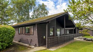 A log cabin with a porch, surrounded by a well-maintained lawn and trees.