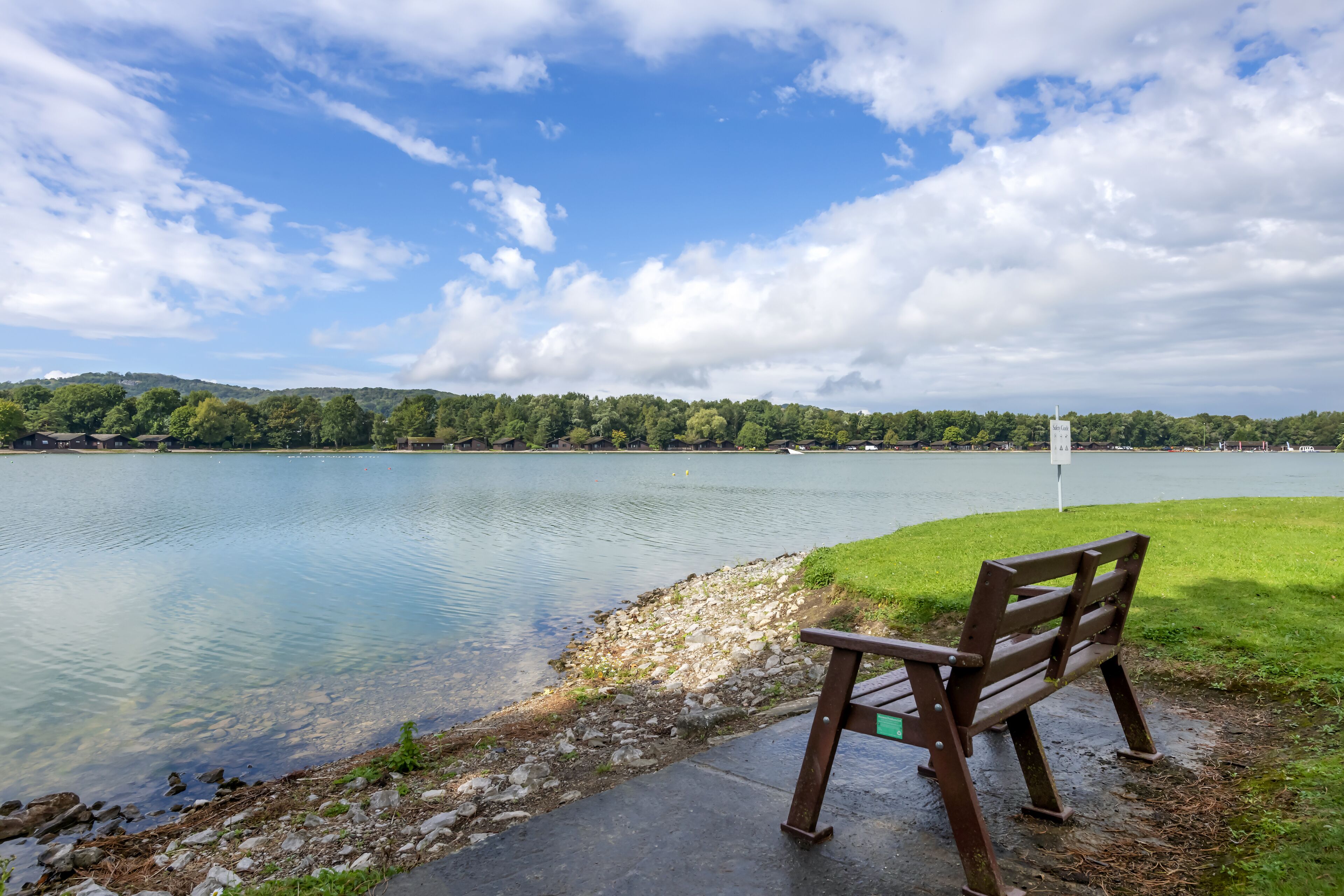 A bench by a lake with a clear view of the water and distant hills.