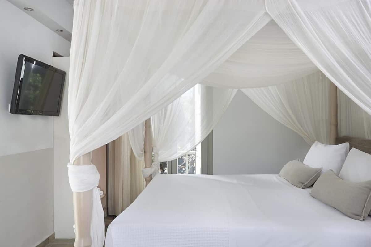 A bedroom with a bed, white curtains, a flat-screen TV, and a window.