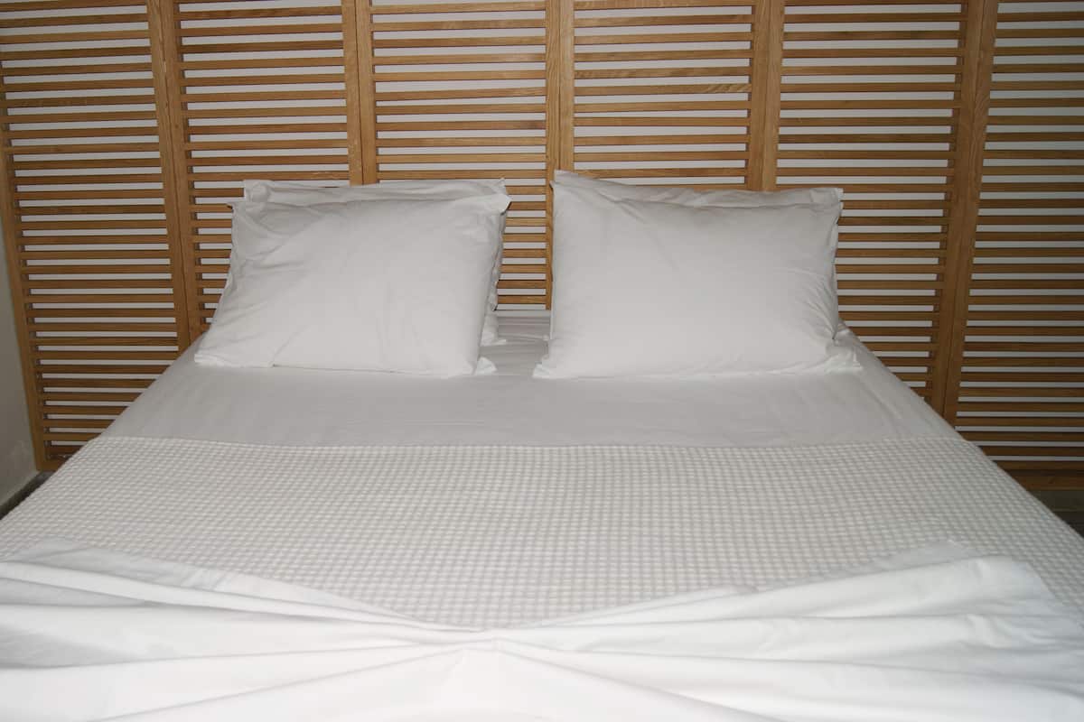 A neatly made bed with white linens and pillows, set against a wooden slat headboard.