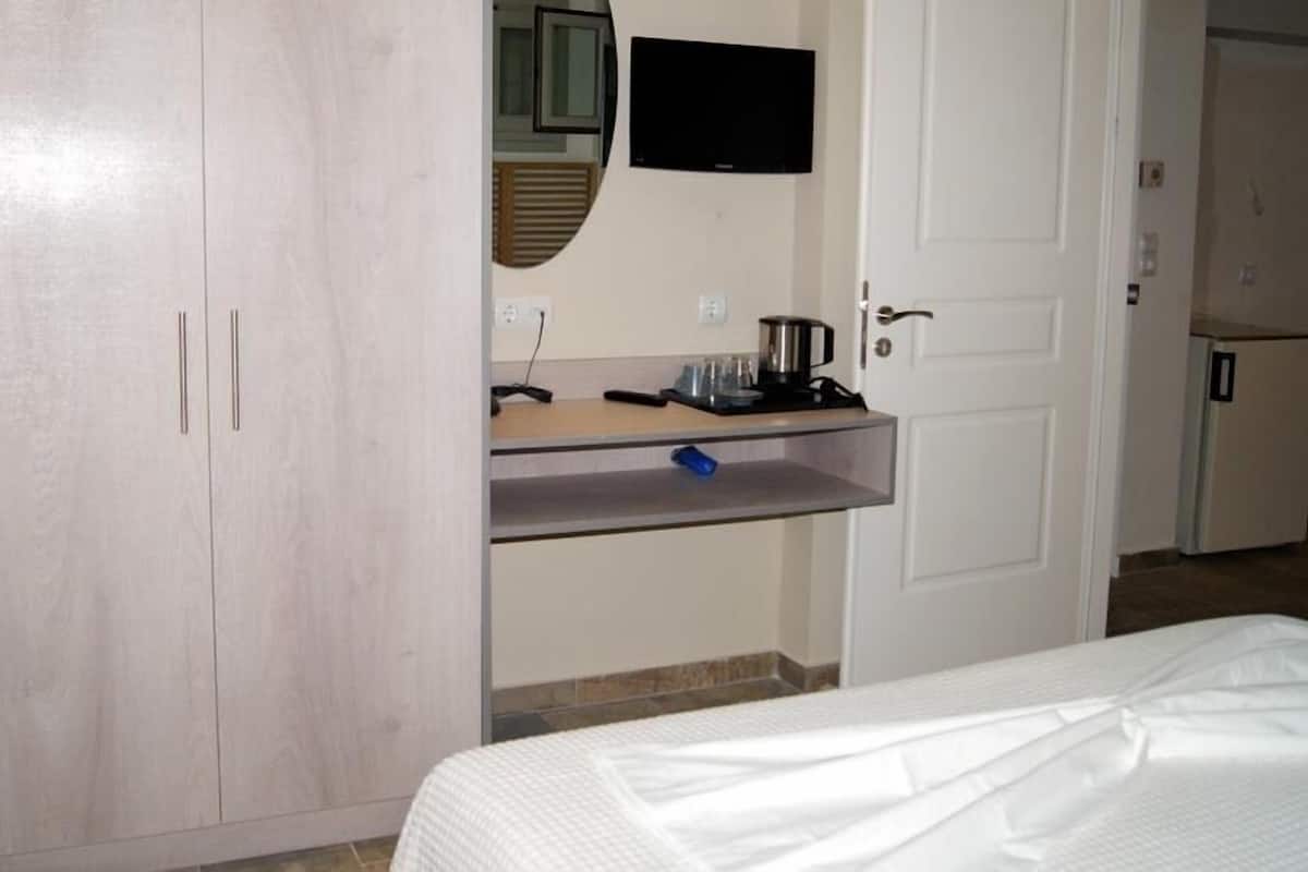 A hotel room with a bed, a wardrobe, a small kitchenette with a coffee maker, and a television mounted on the wall.