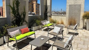 A rooftop terrace with outdoor seating, including a sofa and chairs, surrounded by plants and concrete pillars. - Eos Hotel (Lecce)