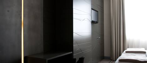 A modern hotel room with a desk, a bed, and a TV mounted on the wall.