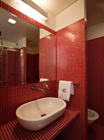 A bathroom with red tiled walls, a white sink, a mirror, and a toilet.